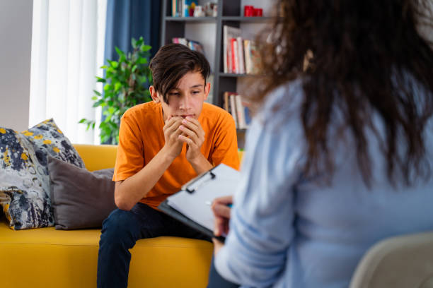 A teenage boy sitting on a couch talking with a therapist during a counseling session
