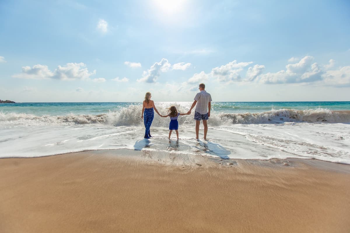 Family holding hands at the beach facing the ocean